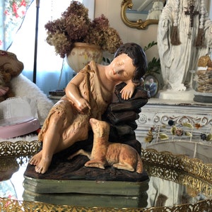 May include: A vintage figurine of a sleeping child holding a lamb. The figurine is made of painted plaster and is in a reclining pose. The child is wearing a simple robe and has a peaceful expression on their face. The lamb is lying next to the child and is also made of painted plaster.