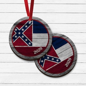 May include: Two round wooden ornaments with a distressed wood finish. Each ornament features a red, white, and blue flag with a white star pattern. The text "2020" is printed on each ornament.