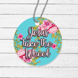 May include: Round blue car charm with a floral pattern and the text "Jesus take the wheel" in pink.