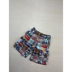 May include: Cargo shorts featuring a multi-colored plaid pattern with shades of red, blue, yellow, green, and white. The shorts include side cargo pockets with flaps, a button closure at the waistband, and a classic straight-leg cut design.