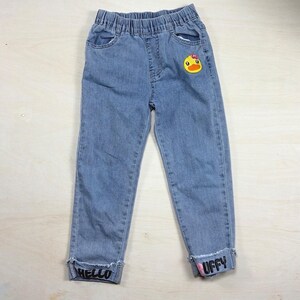 May include: Light blue denim jeans with an elastic waistband, featuring a yellow duck patch on the upper left thigh and frayed cuffs with the text HELLO on the left leg and PUFFY on the right leg in black lettering with a small pink accent.