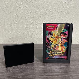 May include: Black rectangular card holder with a Pokemon "Mega Evolution Ascended Heroes" booster bundle. The bundle is in a black frame. A separate black rectangular piece is next to the framed bundle.