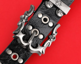May include: Black leather belt with silver-toned metal buckle and decorative studs. The buckle features an ornate design with a hook closure. The belt is studded with silver-colored rivets.