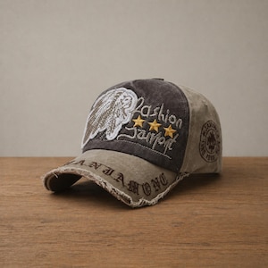 May include: A distressed baseball cap in shades of brown and grey. The cap features embroidered text and a patch with a wing design and the words "Fashion Sport". The brim has a frayed edge, adding to the vintage look.