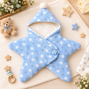 Puede incluir: Una manta de arrullo para bebé con forma de estrella en azul claro con un estampado de estrellas blancas y grises. Incluye una capucha con un pompón blanco, un forro interior blanco con textura y un cierre de botón azul en forma de estrella.