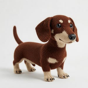 May include: A crocheted dachshund dog in shades of brown and tan. The handmade dog has large, floppy ears, a long body, and short legs. The dog's eyes are black, and it has a black nose. The dog is standing on a white surface.