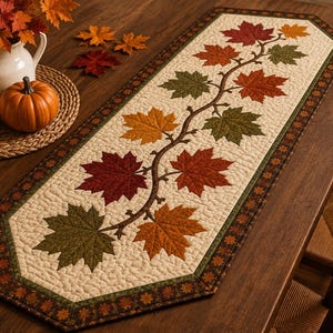 May include: A rectangular table runner featuring a cream-coloured quilted background with a central winding vine pattern adorned with appliqued maple leaves in shades of red, orange, and olive green, finished with a dark brown leaf-patterned border.
