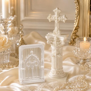 May include: A white, pearlescent decorative set featuring a tall, ornate cross mounted on a fluted column base and a rectangular piece with a detailed gothic arch window design, both crafted with intricate relief patterns and a smooth finish.