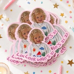 Puede incluir: Un montón de pegatinas rosas troqueladas con la imagen de una joven rubia. Las pegatinas tienen el texto "Look Who's 21" y están rodeadas de confeti, velas y estrellas doradas, creando un ambiente festivo de cumpleaños.