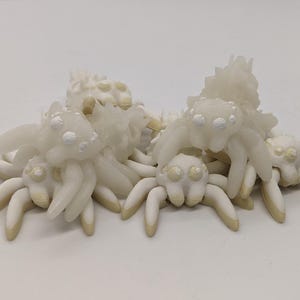 Puede incluir: Un grupo de figuritas de araña de cerámica blanca con detalles brillantes. Las araignées están agrupadas, algunas encima de otras.