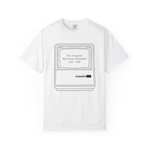 Puede incluir: Camiseta blanca con un gráfico en blanco y negro del ordenador Macintosh original, lanzado en 1984. El texto "The Original Macintosh - Released Year 1984" está impreso en la pantalla. La camiseta tiene cuello redondo.