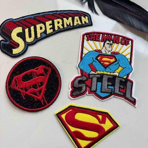 Può includere: Una collezione di toppe ricamate di Superman. Le toppe presentano il logo di Superman, la parola "SUPERMAN" e un'immagine di Superman con la scritta "THE MAN OF STEEL". I colori includono rosso, giallo, blu e nero.
