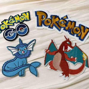 Könnte beinhalten: Gestickte Pokémon-Patches mit Charakteren und Logos. Enthält ein blaues Vaporeon, ein rotes Glurak und das Pokémon GO-Logo. Die Patches haben weiße Ränder und sind auf einem weißen Stoffhintergrund angeordnet.