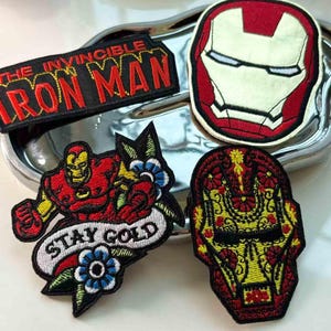 Peut inclure: Collection de patchs brodés Iron Man. Comprend un patch rectangulaire avec le texte "THE INVINCIBLE IRON MAN", un design de masque circulaire, un patch de style tatouage avec le texte "STAY GOLD" et un design de masque inspiré du Jour des Morts.
