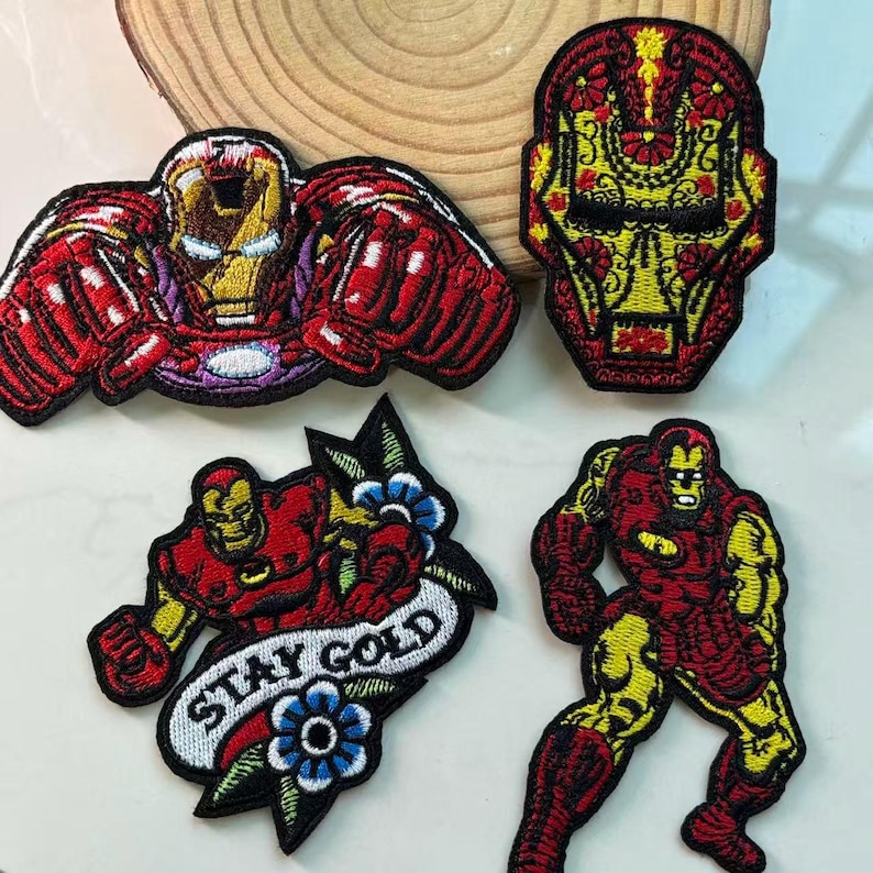 May include: Four embroidered Iron Man patches in various designs. The patches feature Iron Man in different poses and styles, including a Day of the Dead-inspired design. The patches are red, yellow, and black.