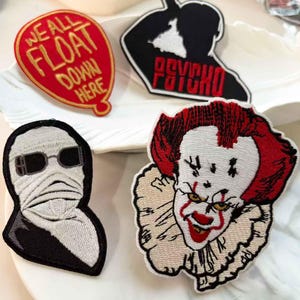 May include: Embroidered patches featuring horror movie themes. Includes a red balloon with "WE ALL FLOAT DOWN HERE" text, a black silhouette with "PSYCHO" text, a monster, and a clown.