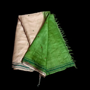May include: A folded textile piece featuring a light beige section with small dark green embroidered accents and a vibrant green section with a textured weave. The green portion includes a decorative border with thin red and dark green lines.