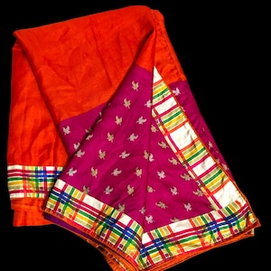 May include: A folded textile featuring a vibrant orange section and a magenta section adorned with small gold bird motifs. The edges are finished with a wide border displaying a multi-colored plaid pattern of blue, green, yellow, and white stripes.