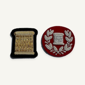 May include: Two embroidered patches. One is a black rectangular patch with a gold thread spool design. The other is a circular red patch featuring a silver thread spool surrounded by a silver embroidered wreath of leaves and branches.