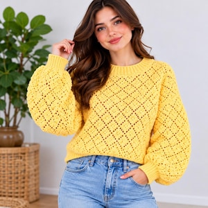 May include: A bright yellow long-sleeve sweater featuring a textured diamond-patterned knit, a round ribbed neckline, and voluminous balloon sleeves with ribbed cuffs, paired with light blue denim jeans.