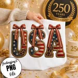 May include: White t-shirt with the word "USA" in red, white, and blue sequined letters. Each letter has a bow on top. The "U" and "A" have a leopard print pattern. The t-shirt is held up by a person.
