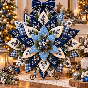 Op de afbeelding: Een stervormige wandhanger van stof met gelaagde, doorgestikte bloemblaadjes in marineblauw, lichtblauw en crème. Het ontwerp bevat ruitpatronen, sneeuwvlokborduurwerk, dennentakjes, kleine blauwe en zilveren ornamenten en dennenappels.