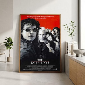 May include: A rectangular movie poster for The Lost Boys featuring a red background and a black and white collage of the cast. The title is printed in white at the bottom, with the tagline Sleep all day. Never grow old. Never die.