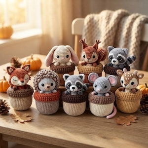 May include: A collection of eight small, crocheted animal figures, including a fox, rabbit, squirrel, raccoon, hedgehog, mouse, and deer, each nestled inside a textured, brown, acorn-shaped crocheted base, arranged on a wooden surface.