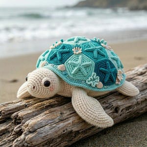 May include: A crocheted sea turtle toy with a cream-coloured head and flippers. The shell is composed of hexagonal patches in shades of teal and turquoise, decorated with small crocheted starfish and seashell motifs in cream and light beige.