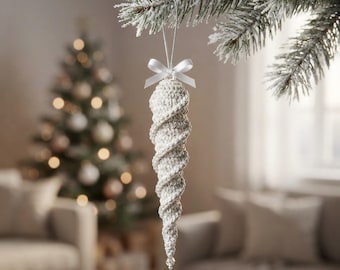 Könnte beinhalten: Ein weißes, gehäkeltes Eiszapfen-Ornament mit Spiralstruktur, das oben mit einer kleinen weißen Satinschleife und einer silbernen Aufhängeschnur versehen ist. Das Ornament läuft spitz zu und ist unten mit einer kleinen, klaren Perle verziert.