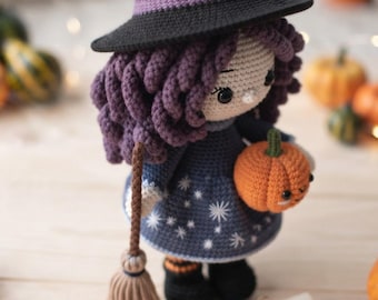 Könnte beinhalten: Eine gehäkelte Puppe als Hexe verkleidet, mit einem schwarzen spitzen Hut mit violettem Band, einem dunkelblauen Kleid mit weißen Sternenmustern und schwarzen Stiefeln. Die Puppe hat lockiges violettes Haar und hält einen kleinen orangefarbenen Kürbis.