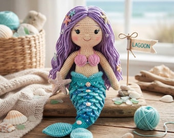 Könnte beinhalten: Eine gehäkelte Meerjungfrauenpuppe mit langem violettem Garnhaar, das mit kleinen Seesternen verziert ist. Die Puppe trägt ein rosafarbenes muschelförmiges Oberteil und einen blau-türkisfarbenen Schwanz mit Schuppenmuster. Ein Schild trägt die Aufschrift LAGOON.
