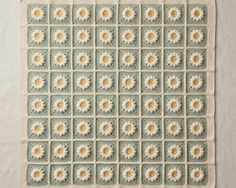 Könnte beinhalten: Eine quadratische Häkeldecke mit einem sich wiederholenden Gänseblümchenmuster. Jedes Quadrat besteht aus einem salbeigrünen Hintergrund mit einer weißblättrigen Blume und einem gelben Zentrum. Das Stück ist mit einem cremefarbenen Häkelrand eingefasst.