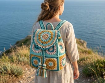 Könnte beinhalten: Ein gehäkelter Rucksack mit einem mandala-inspirierten Muster in den Farben Petrol, Senfgelb und zartem Rosa. Die Tasche verfügt über einen Klappverschluss mit zwei langen geflochtenen Kordeln, die in dekorativen Quasten enden, sowie geflochtene Träger.