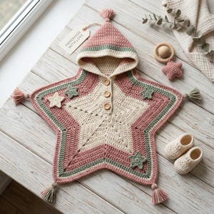 May include: A star-shaped hooded crochet poncho in dusty rose, cream, and sage green. The garment features a central cream star, three wooden buttons, and small star appliqués. Tassels adorn the points, and a tag reads HANDMADE WITH LOVE.