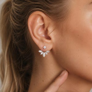 May include: A silver-toned ear jacket earring featuring a small round stud at the front and a fan-shaped attachment behind the earlobe, adorned with multiple marquise-cut and round-cut clear stones arranged in a symmetrical, layered design.