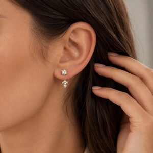 May include: A gold-toned ear jacket earring featuring a single round brilliant-cut stone stud at the front and a dangling, leaf-shaped attachment at the back, composed of three small marquise-cut stones arranged in a cluster beneath the earlobe.