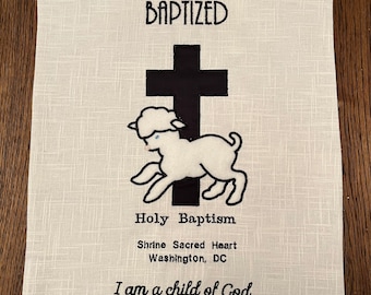 Könnte beinhalten: Weißer bestickter Stoff mit einem schwarzen Kreuz und einem weißen Lamm. Oben steht der Text "BAPTIZED", gefolgt von "Holy Baptism", "Shrine Sacred Heart", "Washington, DC" und "I am a child of God".