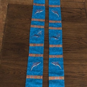 K&ouml;nnte beinhalten: Eine blaue Stola mit Delfin-Stickerei und dekorativen Quadraten. Die Stola zeigt eine Brezel und die jamaikanische Flagge. Der Text "Sept 5, 2021" ist ebenfalls sichtbar.