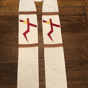 K&ouml;nnte beinhalten: Cremefarbene liturgische Stola mit einem goldenen Kreuz oben und zwei stilisierten roten und goldenen Kreuzen. Die Stola hat eine braune Zierleiste und ist aus einem strukturierten Stoff gefertigt.