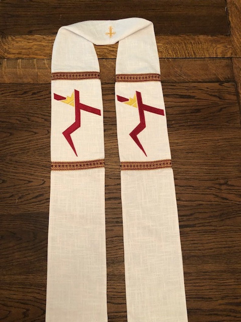 K&ouml;nnte beinhalten: Cremefarbene liturgische Stola mit einem goldenen Kreuz oben und zwei stilisierten roten und goldenen Kreuzen. Die Stola hat eine braune Zierleiste und ist aus einem strukturierten Stoff gefertigt.