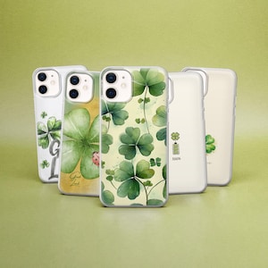 May include: A collection of five phone cases with various designs featuring green shamrocks and clovers. Some cases have text, a ladybug, and a battery icon. The cases are on a light green background.