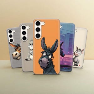 May include: Five phone cases with cartoon donkey designs. The cases showcase donkey illustrations with diverse expressions and styles. The cases are in shades of grey, orange, and blue, set against a neutral background. The cases are designed for a smartphone.