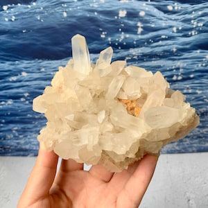 May include: A cluster of translucent, clear quartz crystals with sharp, pointed terminations. The mineral formation features multiple jagged points radiating from a central base, displaying a natural, crystalline structure with light-reflecting facets.