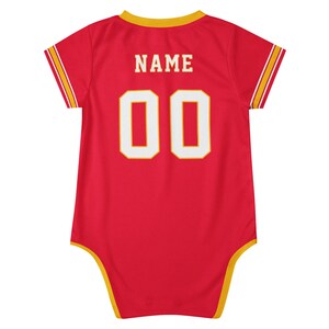 May include: A red short-sleeved bodysuit featuring yellow trim on the neckline, sleeve cuffs, and leg openings. The back displays the word NAME in white block letters above the number 00, which is also in white with a yellow outline.