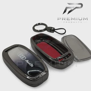 May include: A black car key case with the Audi logo, a key ring, and a detached cover. The interior of the case is lined with red fabric. The key case is designed to protect the car key.