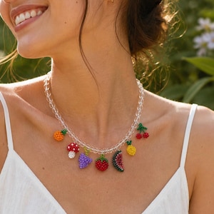 May include: A necklace with beaded fruit and mushroom charms. The charms include an orange pineapple, a red and white mushroom, a purple flower, a red strawberry, a watermelon slice, a yellow pineapple, and red cherries. The necklace is made of clear beads.