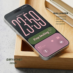 Könnte beinhalten: Ein silbernes Smartphone zeigt ein benutzerdefiniertes Hintergrundbild mit schwarzem Hintergrund und großen rosa Zahlen, die die Uhrzeit anzeigen. Der Bildschirm zeigt auch den Text "Keep Smiling" und Wetterinformationen. Das Telefon liegt in einem Holztablett.