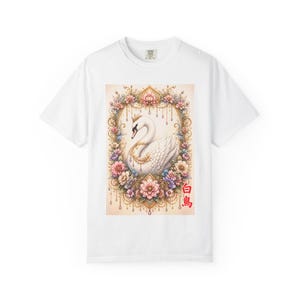 以下が含まれることがあります： 王冠をつけた白鳥の詳細なイラストが描かれた白いTシャツ。花柄のフレームで囲まれています。デザインにはピンク、紫、金のアクセントがあり、日本語のテキストが添えられています。Tシャツはクラシックなクルーネックです。
