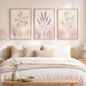 以下が含まれることがあります： 水彩画の植物イラストが描かれた3枚の額入りウォールアートプリントセット。左のプリントにはピンクの花、中央には紫色のラベンダーの小枝、右には繊細な葉が描かれており、すべて柔らかなパステルカラーの背景に配置されています。